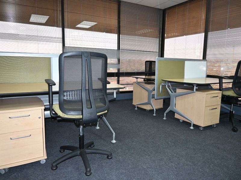 A professional office space featuring carpeted flooring, suspended ceilings with recessed lighting, and large windows fitted with venetian blinds.