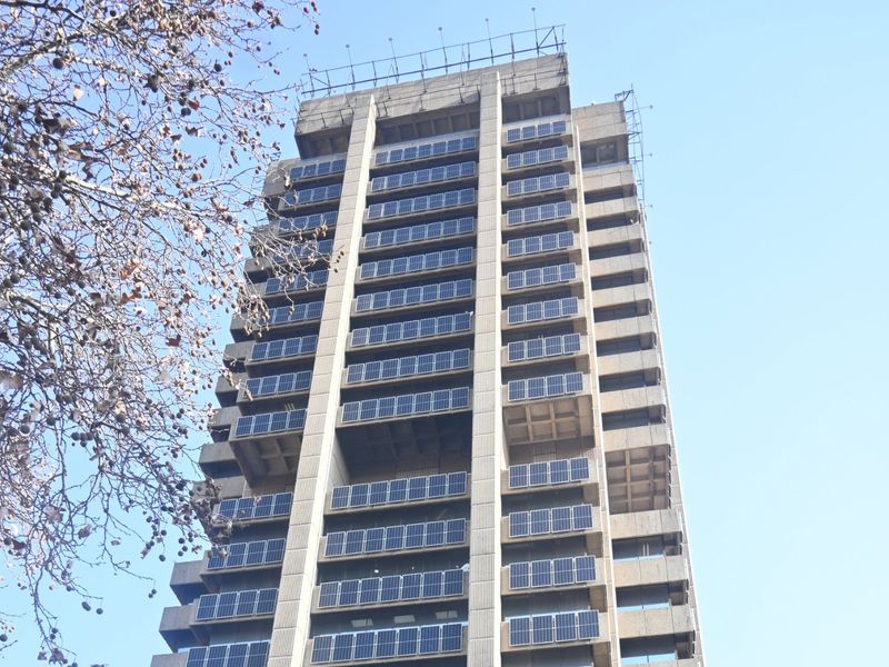A high-rise commercial building featuring a concrete facade and extensive solar panel installations on the exterior balconies.