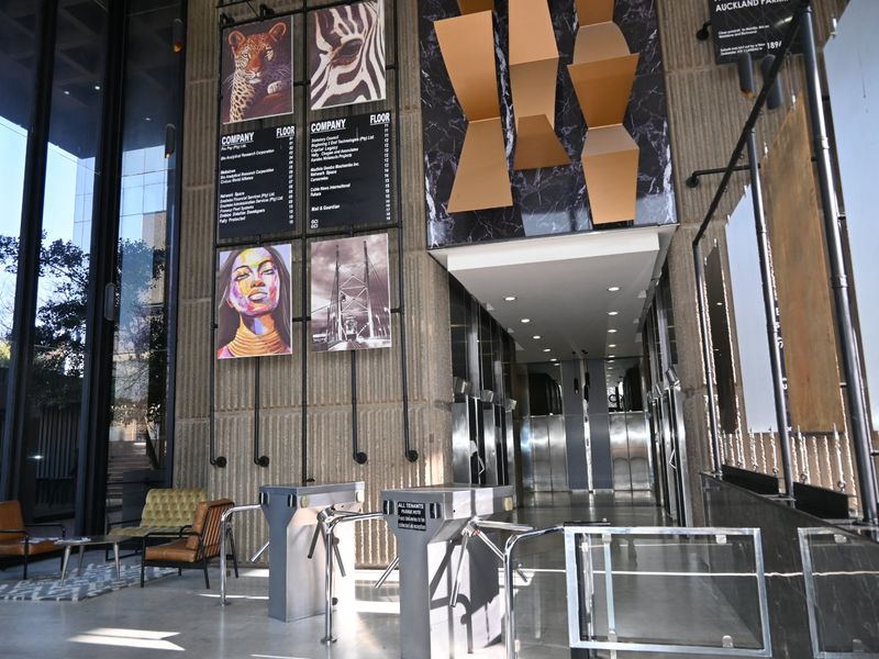 Modern commercial building lobby featuring high ceilings, textured concrete and marble finishes, security turnstiles, and stainless steel elevator access.