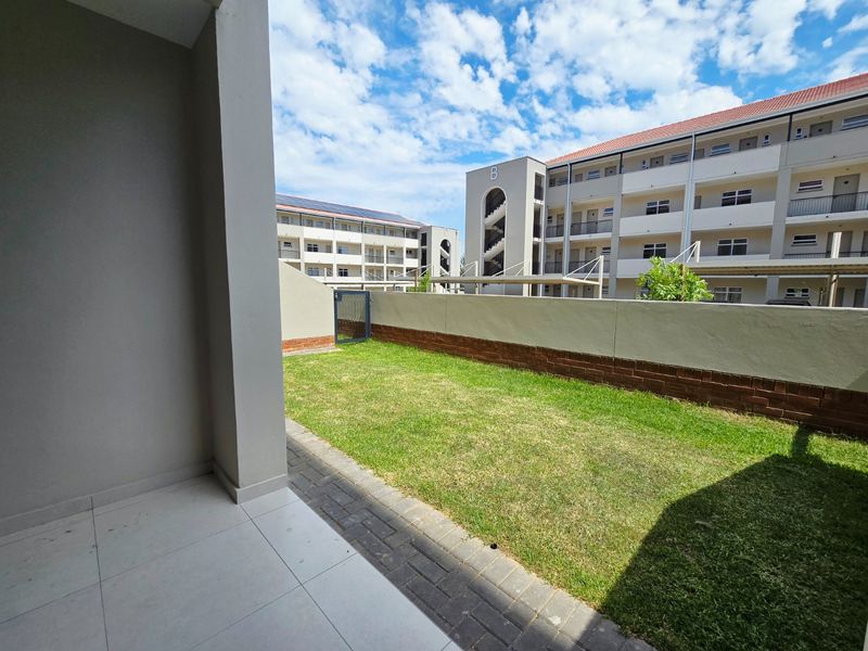 A private ground floor patio area featuring tiled flooring, a small lawn, and a brick boundary wall within an apartment complex.