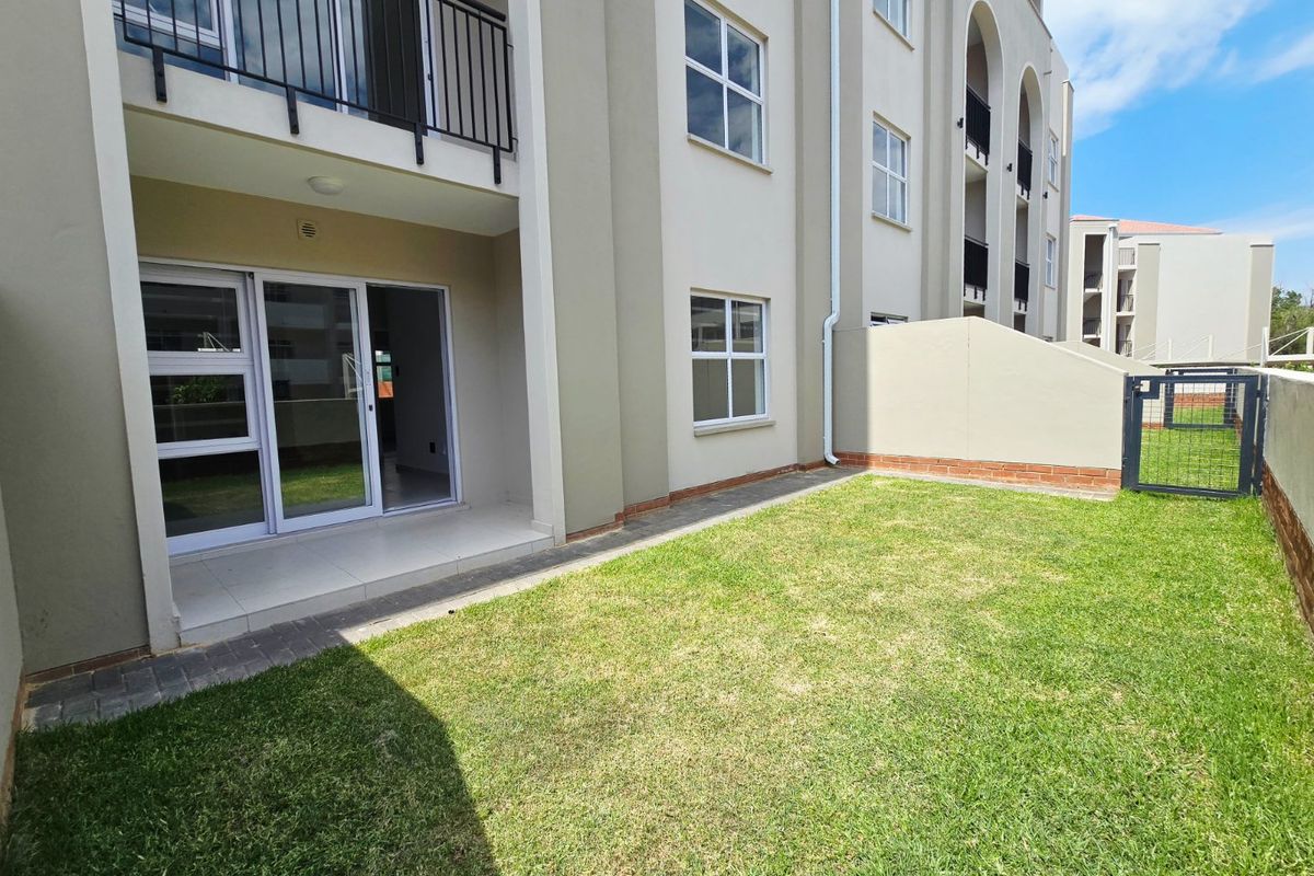 A ground floor apartment exterior featuring a private garden, paved patio area, and sliding glass doors leading into the living space.