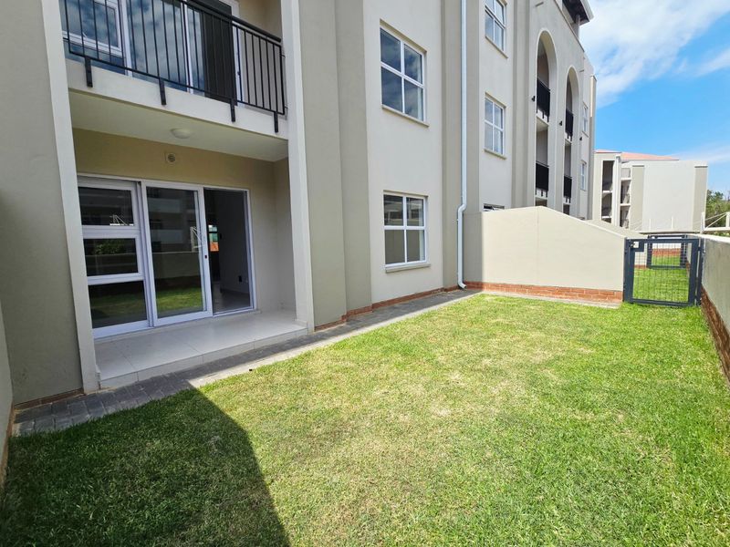 A ground floor apartment exterior featuring a private garden, paved patio area, and sliding glass doors leading into the living space.