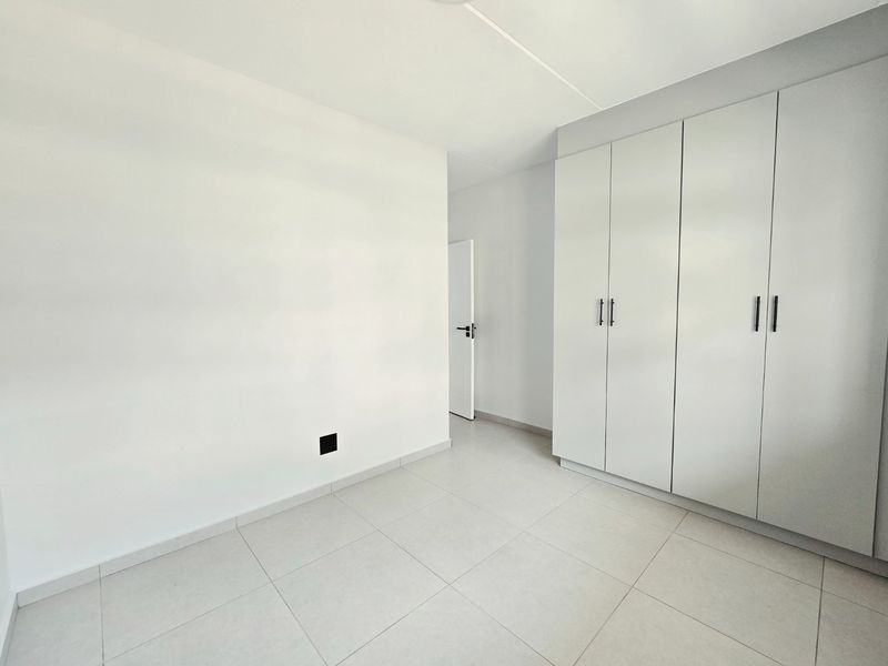A bright, empty bedroom featuring neutral tiled flooring and modern built-in cupboards with clean white finishes.