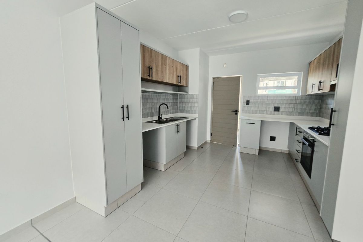 Modern kitchen featuring light grey cabinetry, wood-look upper cabinets, tiled backsplash, built-in oven, gas hob, and neutral floor tiles in an open-plan layout.
