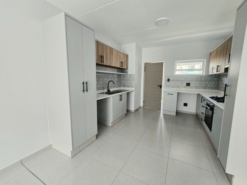 Modern kitchen featuring light grey cabinetry, wood-look upper cabinets, tiled backsplash, built-in oven, gas hob, and neutral floor tiles in an open-plan layout.