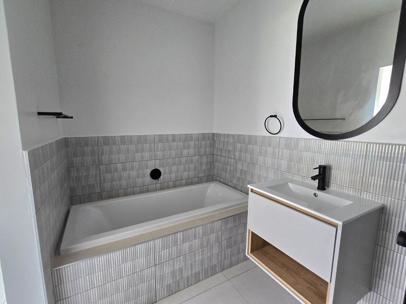 Modern bathroom featuring a built-in bathtub with textured tile surround, a contemporary wall-mounted vanity with integrated sink, and stylish black matte fixtures.