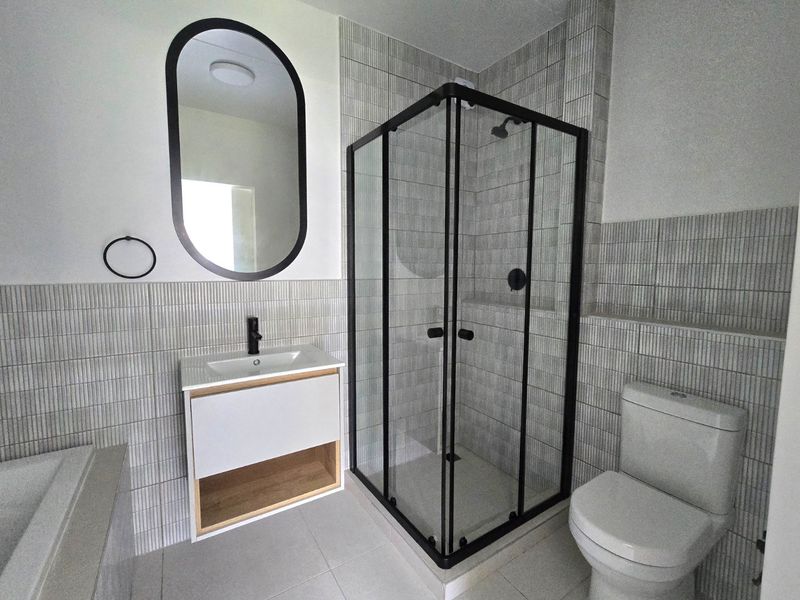 Modern bathroom featuring a glass shower enclosure, contemporary vanity with basin, wall-mounted mirror, and toilet, finished with stylish vertical wall tiling.