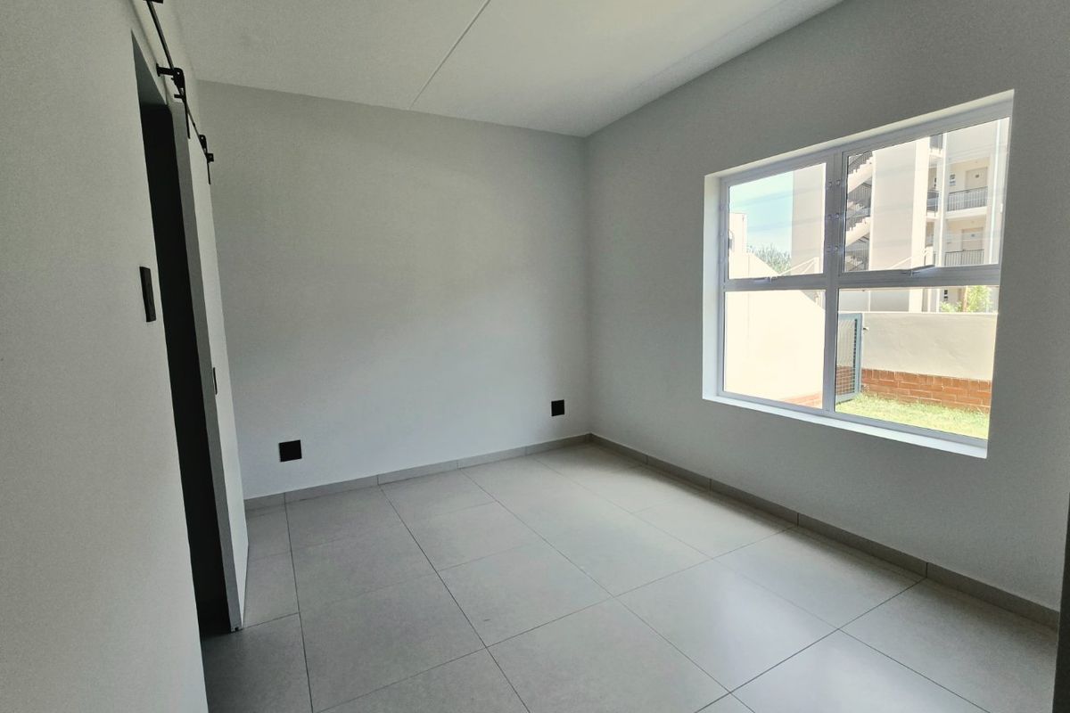 A bright, empty bedroom featuring modern tiled flooring, a sliding barn door, and a large window providing natural light.