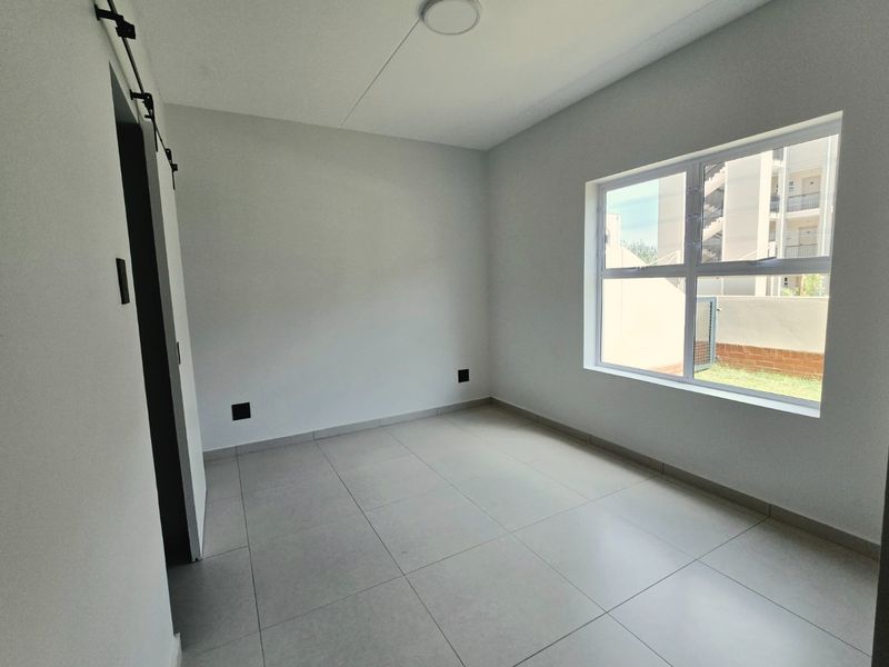 A bright, empty bedroom featuring modern tiled flooring, a sliding barn door, and a large window providing natural light.