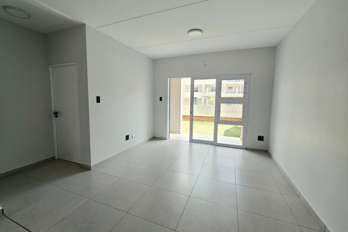 A bright, empty living room featuring neutral tiled flooring and a large sliding glass door providing access to an outdoor area.