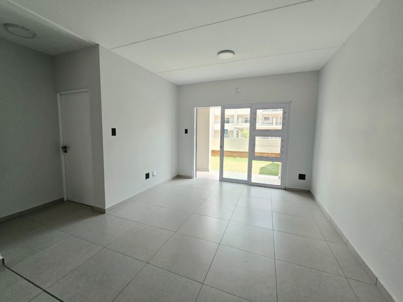 A bright, empty living room featuring neutral tiled flooring and a large sliding glass door providing access to an outdoor area.