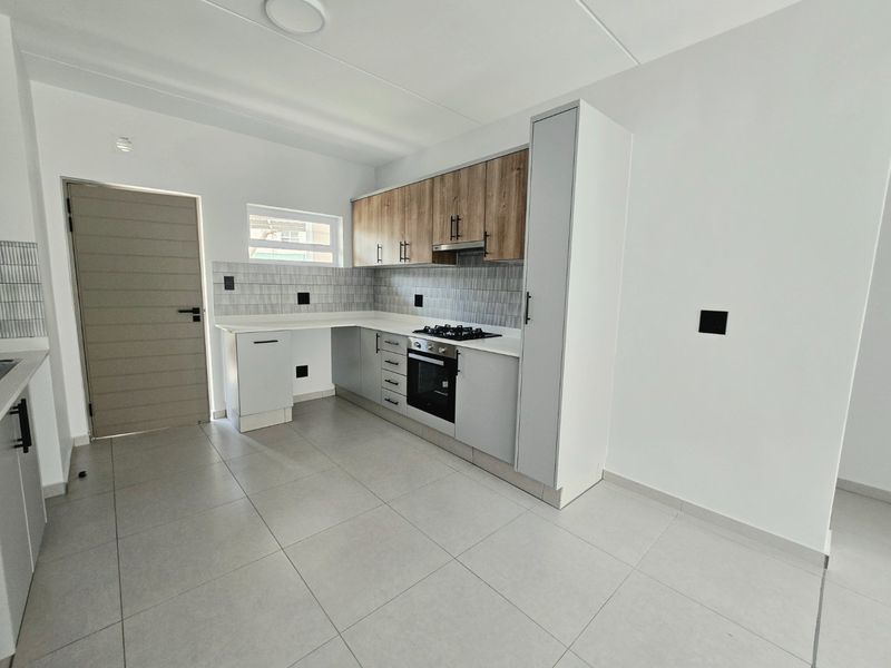 Modern kitchen featuring two-tone cabinetry, stone countertops, built-in gas hob, electric oven, extractor fan, and neutral tiled flooring.
