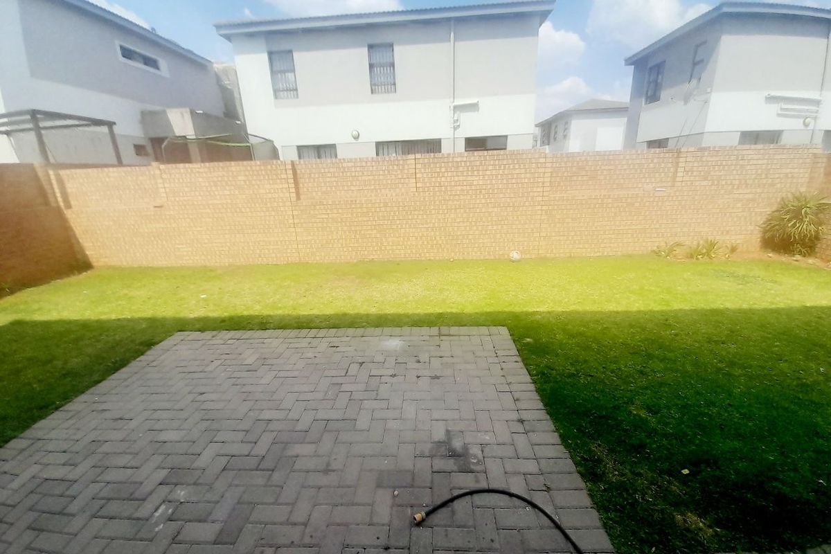 A private rear garden featuring a paved patio area and a well-maintained lawn enclosed by a brick boundary wall.