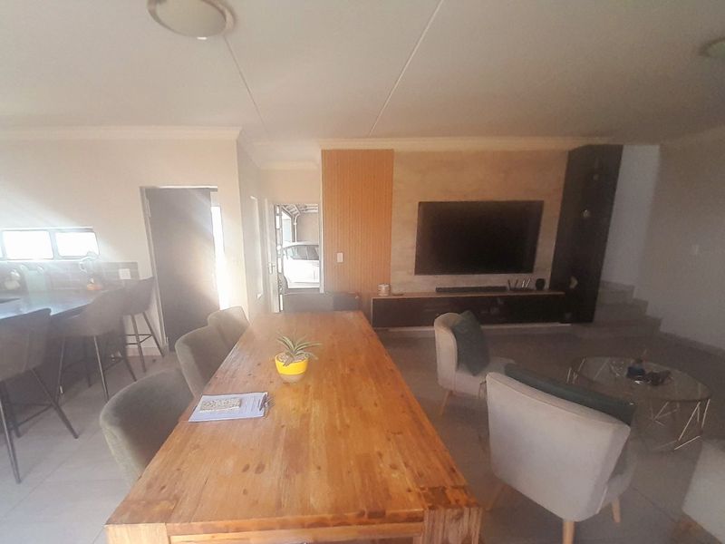 Spacious open-plan living and dining area featuring modern tiled floors, a feature wall with built-in cabinetry, and a functional kitchen island.