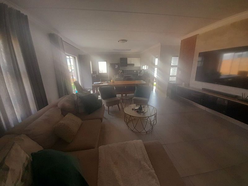 Spacious open-plan living area featuring large format floor tiles, a modern media wall with timber slat detailing, and integrated lighting.