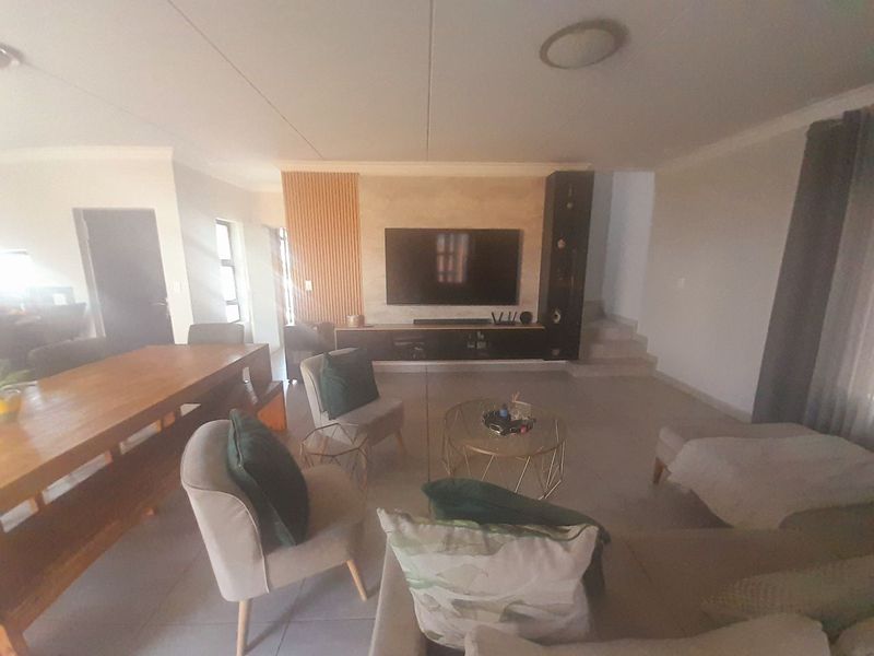Spacious open-plan living area featuring a modern media wall with slatted wood accents, tiled flooring, and an integrated staircase.