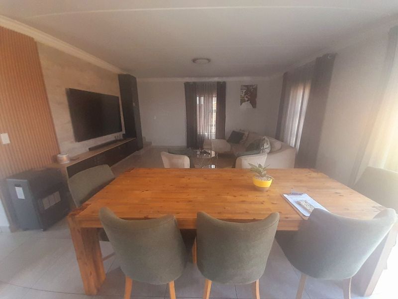 An open-plan living and dining area featuring tiled flooring, coving, and a built-in media unit, offering a functional space for relaxation and dining.