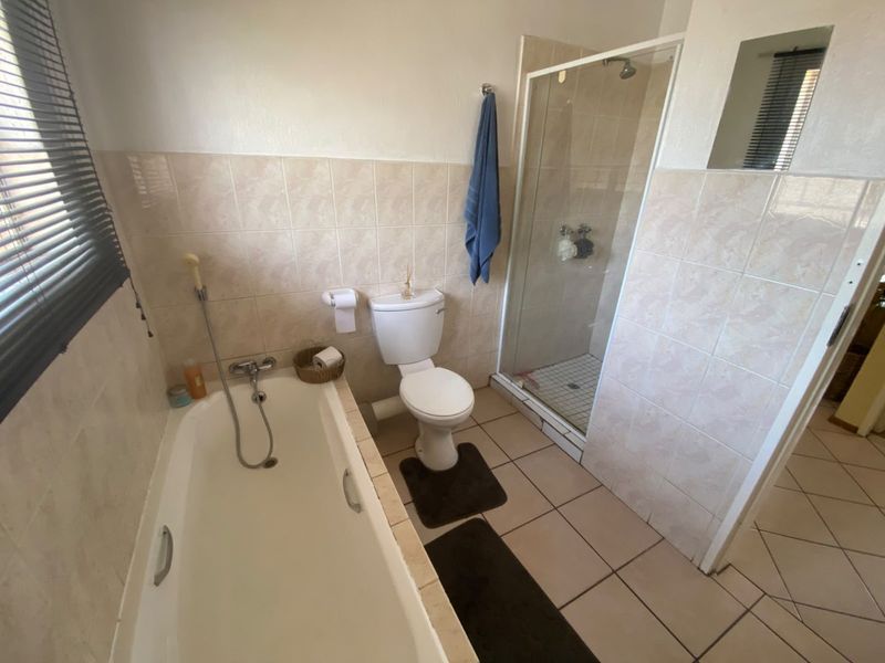 A functional bathroom featuring a bathtub, separate shower enclosure, and toilet with neutral wall and floor tiling.