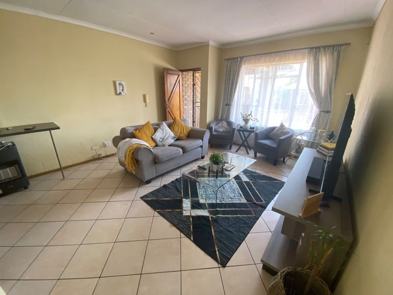 A spacious living room featuring tiled flooring, neutral wall tones, and large windows that provide ample natural light.