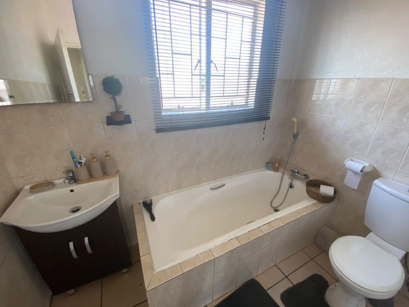 A functional bathroom featuring a vanity basin, bathtub with handheld shower attachment, and a standard toilet, finished with neutral wall and floor tiling.