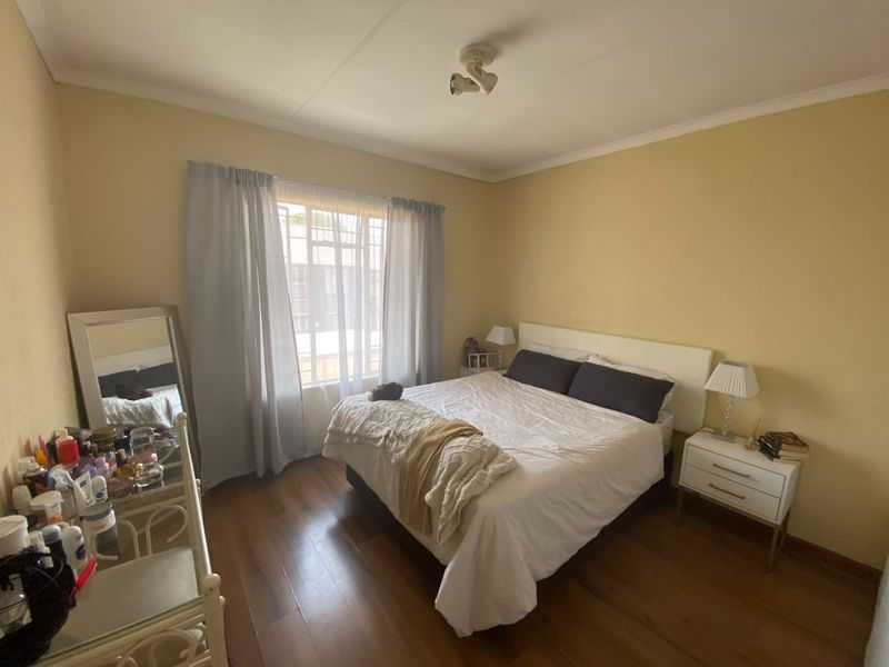 A well-lit bedroom featuring laminate flooring, a ceiling-mounted spotlight fixture, and a window fitted with security bars.