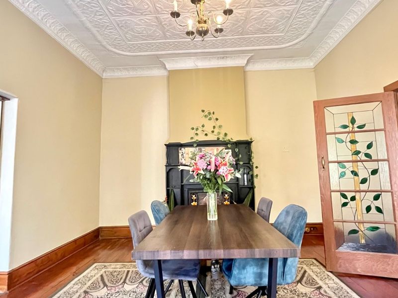 Elegant dining room featuring a classic pressed metal ceiling, ornate cornice, fireplace mantel, and a beautiful stained glass feature door.