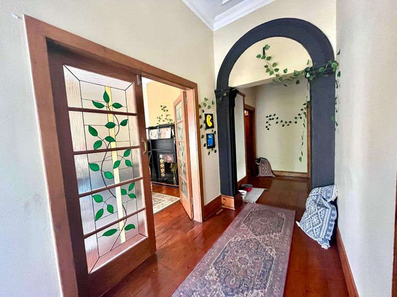 A character-filled hallway featuring polished timber flooring, a decorative archway, and a classic stained glass door leading into an adjoining room.