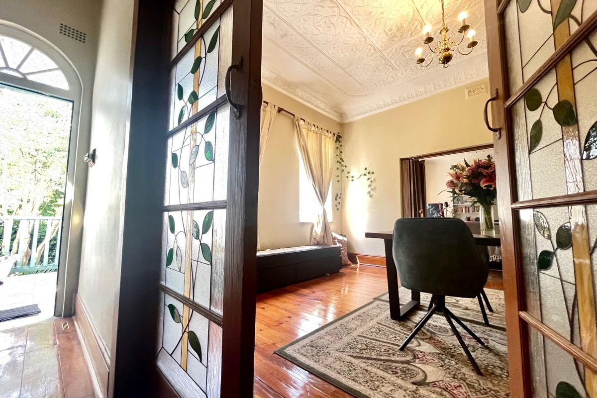 Elegant living area featuring original pressed metal ceilings, ornate ceiling roses, and beautiful stained glass sliding doors opening onto a bright hallway.