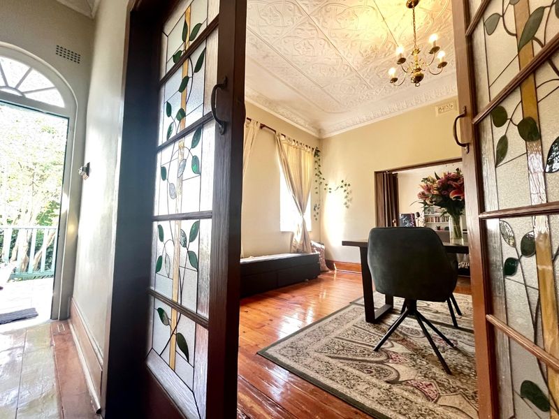 Elegant living area featuring original pressed metal ceilings, ornate ceiling roses, and beautiful stained glass sliding doors opening onto a bright hallway.