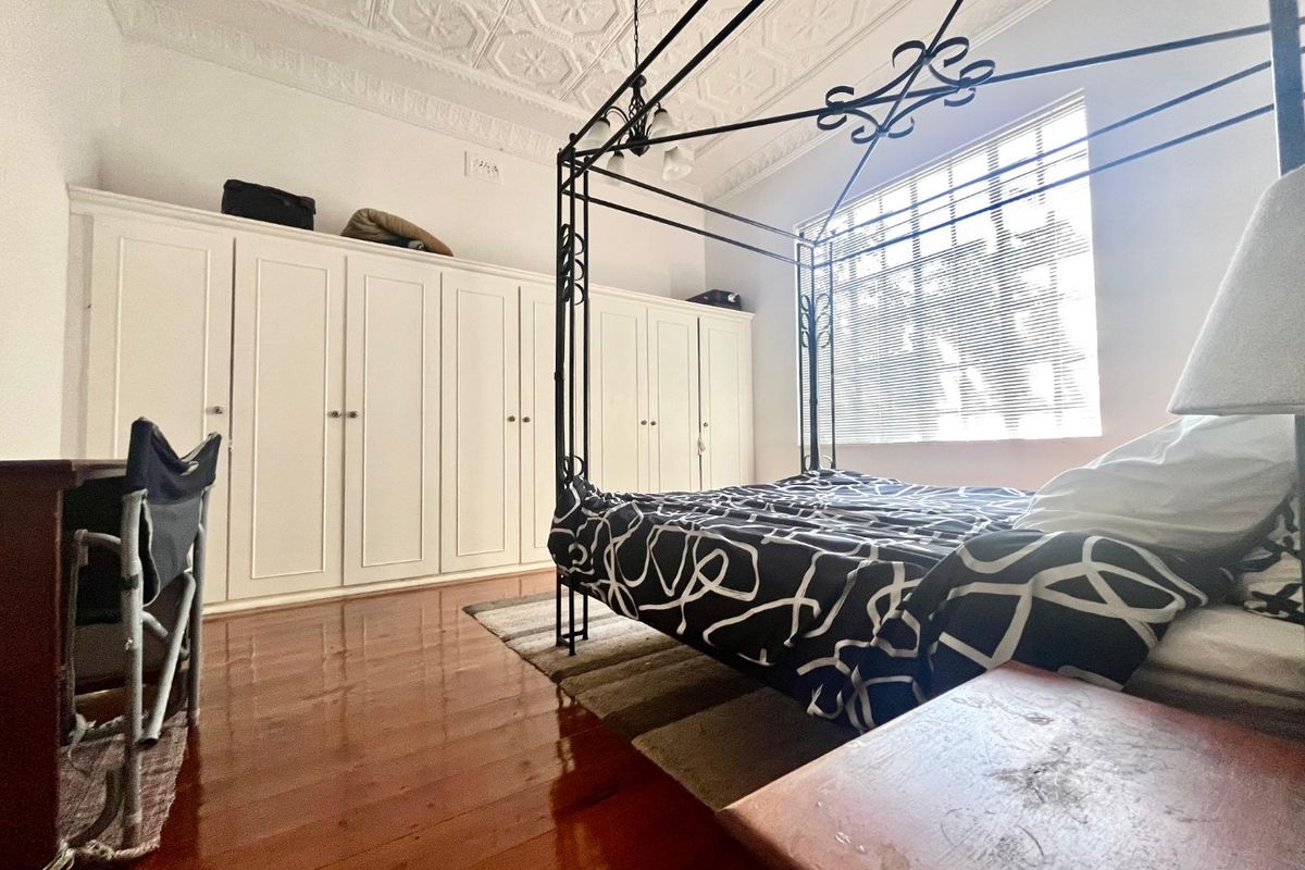 Spacious bedroom featuring classic pressed metal ceilings, ornate cornicing, polished hardwood floors, and extensive built-in wardrobe storage.