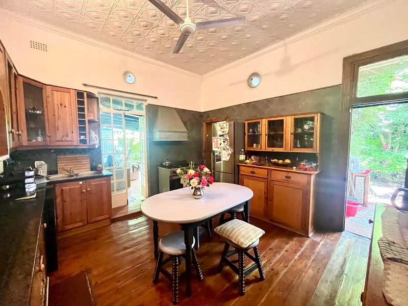 A rustic kitchen featuring traditional wooden cabinetry, a pressed metal ceiling, and hardwood floors, with direct access to an outdoor patio area.