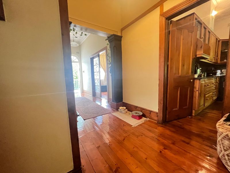 A traditional hallway featuring polished timber flooring, classic timber door frames, and an architectural archway leading towards the entrance.