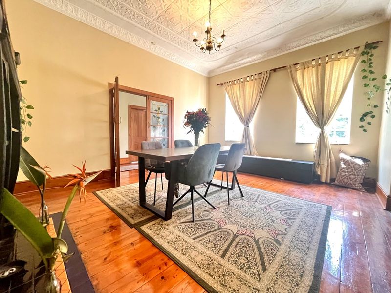 Spacious dining room featuring original pressed metal ceilings, polished timber flooring, and elegant stained glass double doors leading to the hallway.