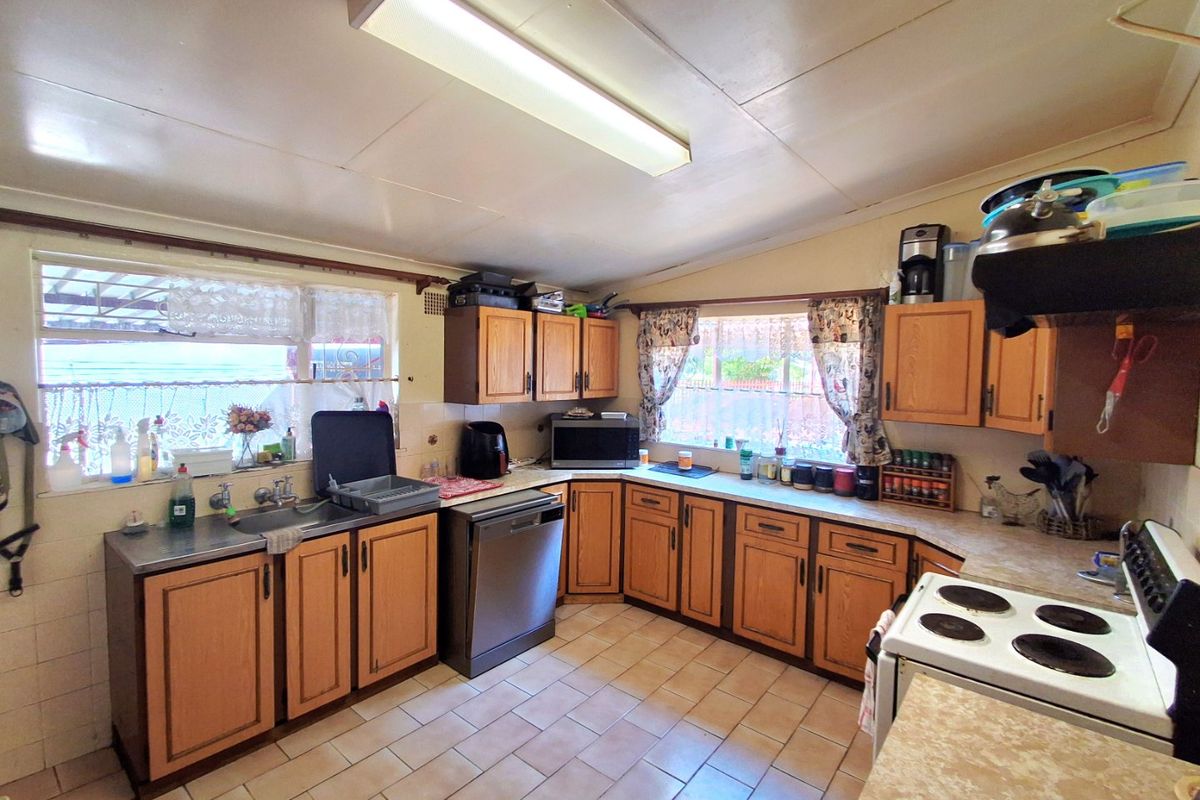 A functional kitchen featuring timber cabinetry, laminate countertops, tiled flooring, and a built-in electric stove, offering potential for modern updates.
