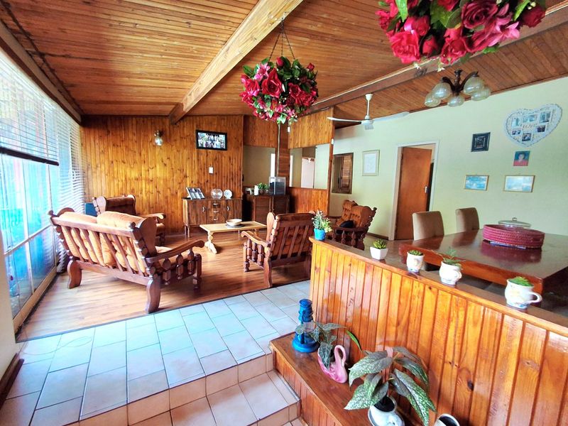 Spacious open-plan living and dining area featuring timber-clad walls and ceilings, exposed beams, and a combination of tiled and timber flooring.