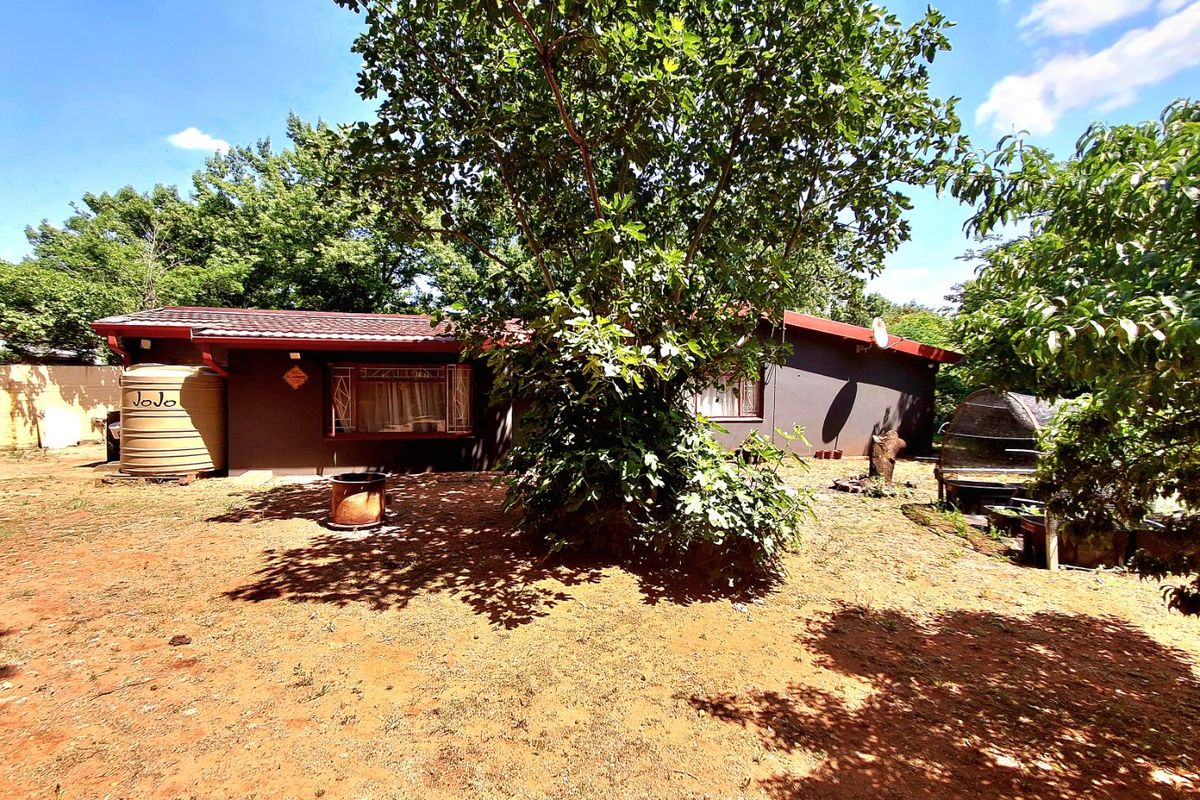 Rear view of the property featuring a dark-painted exterior, tiled roof, security window bars, and a large water storage tank in the garden area.