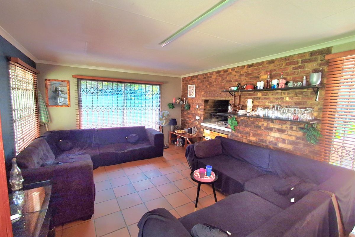 Spacious living area featuring exposed brickwork, a built-in braai, tiled flooring, and large windows with security gates and venetian blinds.