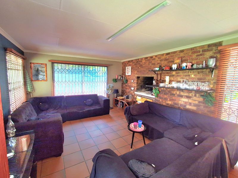 Spacious living area featuring exposed brickwork, a built-in braai, tiled flooring, and large windows with security gates and venetian blinds.