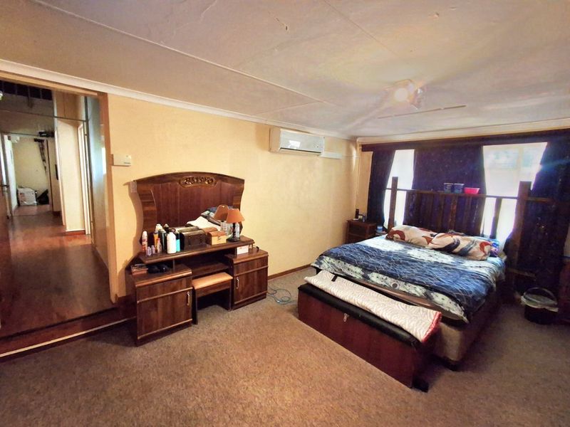 A bedroom featuring carpeted flooring, a ceiling fan, and a wall-mounted split-system air conditioner, with visible signs of wear on the ceiling.