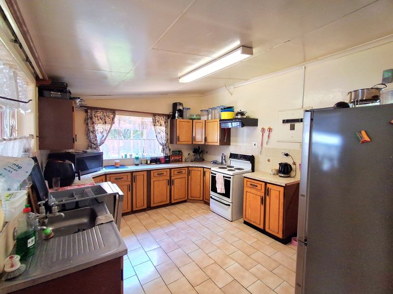 A functional kitchen featuring wooden cabinetry, tiled flooring, a freestanding stove with extractor fan, and a stainless steel sink with tiled backsplash.