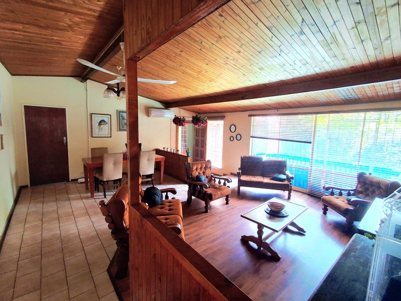 Spacious open-plan living and dining area featuring warm timber ceilings, a mix of tiled and laminate flooring, and large windows providing natural light.