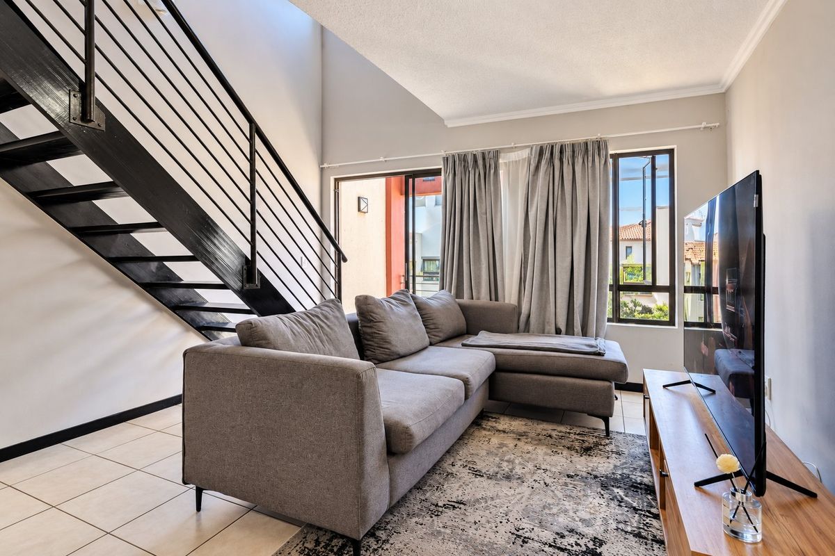 A bright living room featuring a modern metal staircase, tiled flooring, and large sliding glass doors that provide access to an outdoor area.