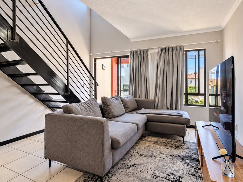 A bright living room featuring a modern metal staircase, tiled flooring, and large sliding glass doors that provide access to an outdoor area.