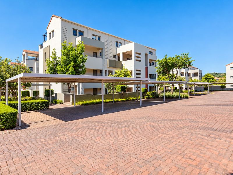 Exterior view of a modern apartment complex featuring paved parking areas with covered bays and well-maintained landscaped garden beds.