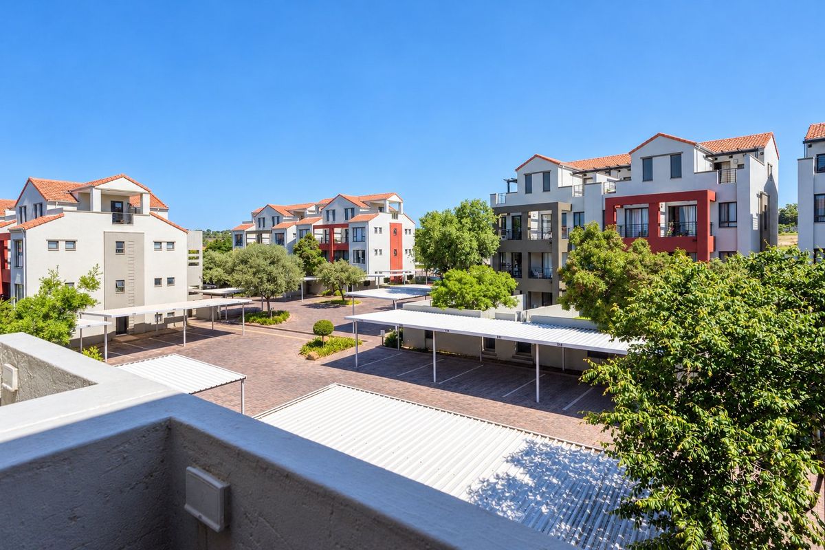 An elevated view of the apartment complex grounds, featuring paved parking bays with covered carports and well-maintained landscaped areas between the residential buildings.