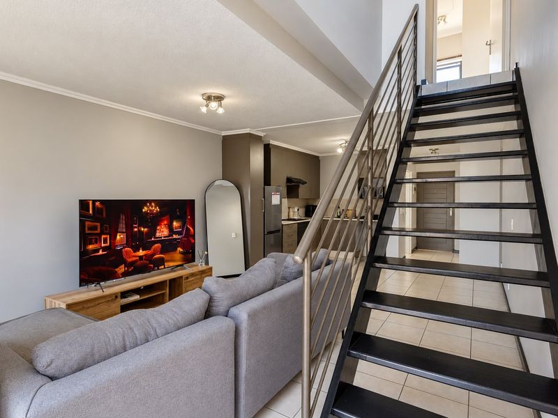 Open plan living area featuring a modern staircase with metal balustrade, tiled flooring, and a compact kitchen with built-in cabinetry.