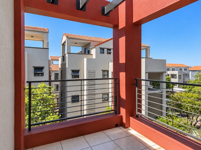 A spacious covered balcony featuring tiled flooring, a modern metal balustrade, and a structural pergola, offering views of the surrounding apartment complex.