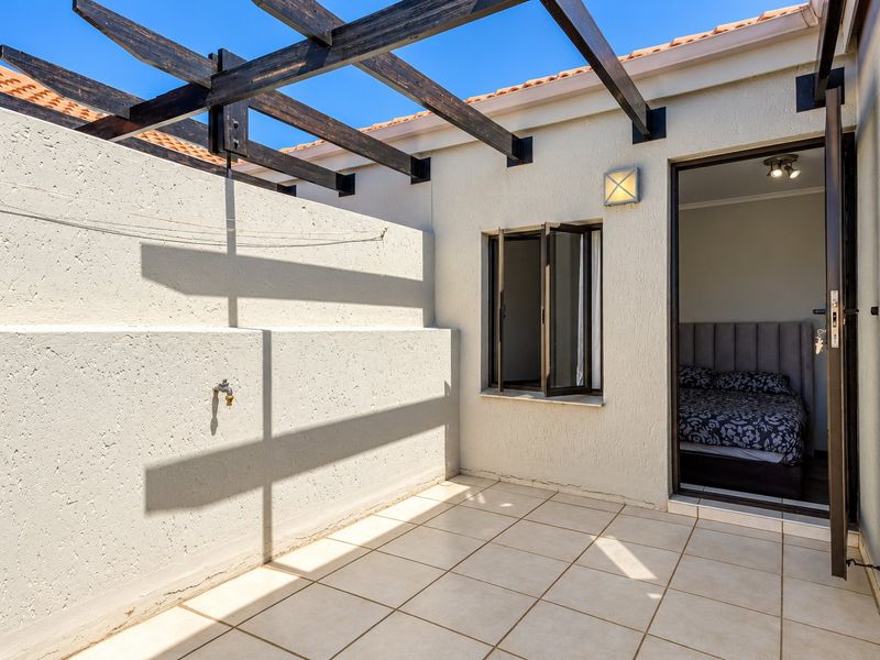 A private tiled patio area featuring a timber pergola, outdoor tap, and direct access to the bedroom.