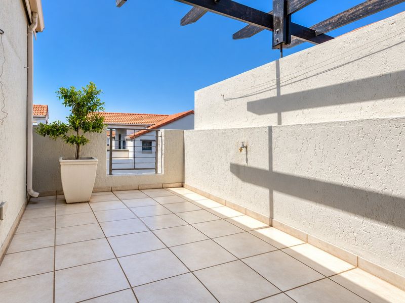 A clean, open-air balcony featuring tiled flooring, a timber pergola structure, and a convenient exterior wall tap.