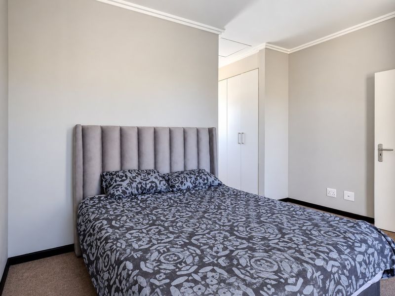 A well-maintained bedroom featuring neutral walls, carpeted flooring, coving, and built-in storage cupboards.